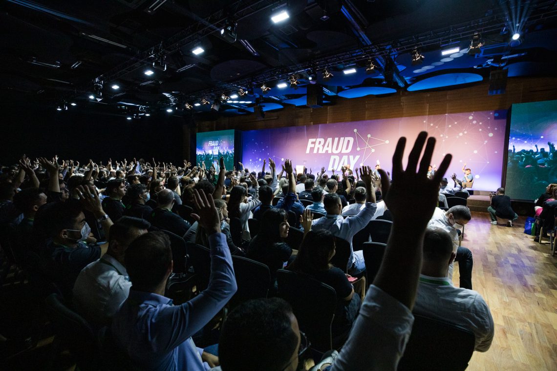 A imagem retrata o evento Fraud Day 2022, promovido pela konduto. Na foto, há um painel à frente e pessoas sentadas na platéia com mãos levantadas.