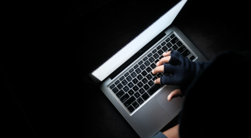 Pessoa vestindo luvas e utilizando um notebook, remetendo ao crime cibernético Account Farming.