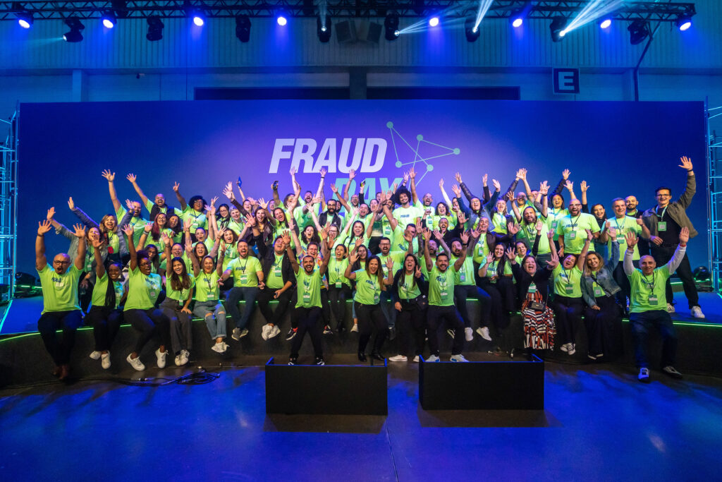 A foto mostra o time que organizou o evento com cerca de 107 pessoas em cima do palco, todas vestindo blusa verde neon, com as mãos para o alto e sorrindo. 