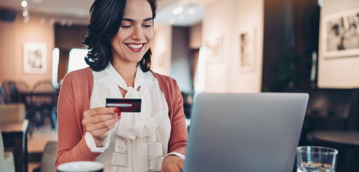 Mulher sorridente em frente ao computador, segurando um cartão, remetendo a autenticação e prevenção à fraude.