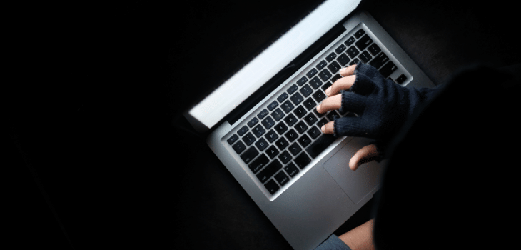 Arte ilustrativa mostra uma pessoa mexendo no computador com o fundo escuro, remetendo as fraudes em transações online.