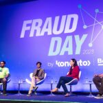 Foto colorida de um dos painéis do Fraud Day. A imagem mostra quatro pessoas sentadas, uma delas com um microfone. Há um fundo azul escrito "Fraud Day".